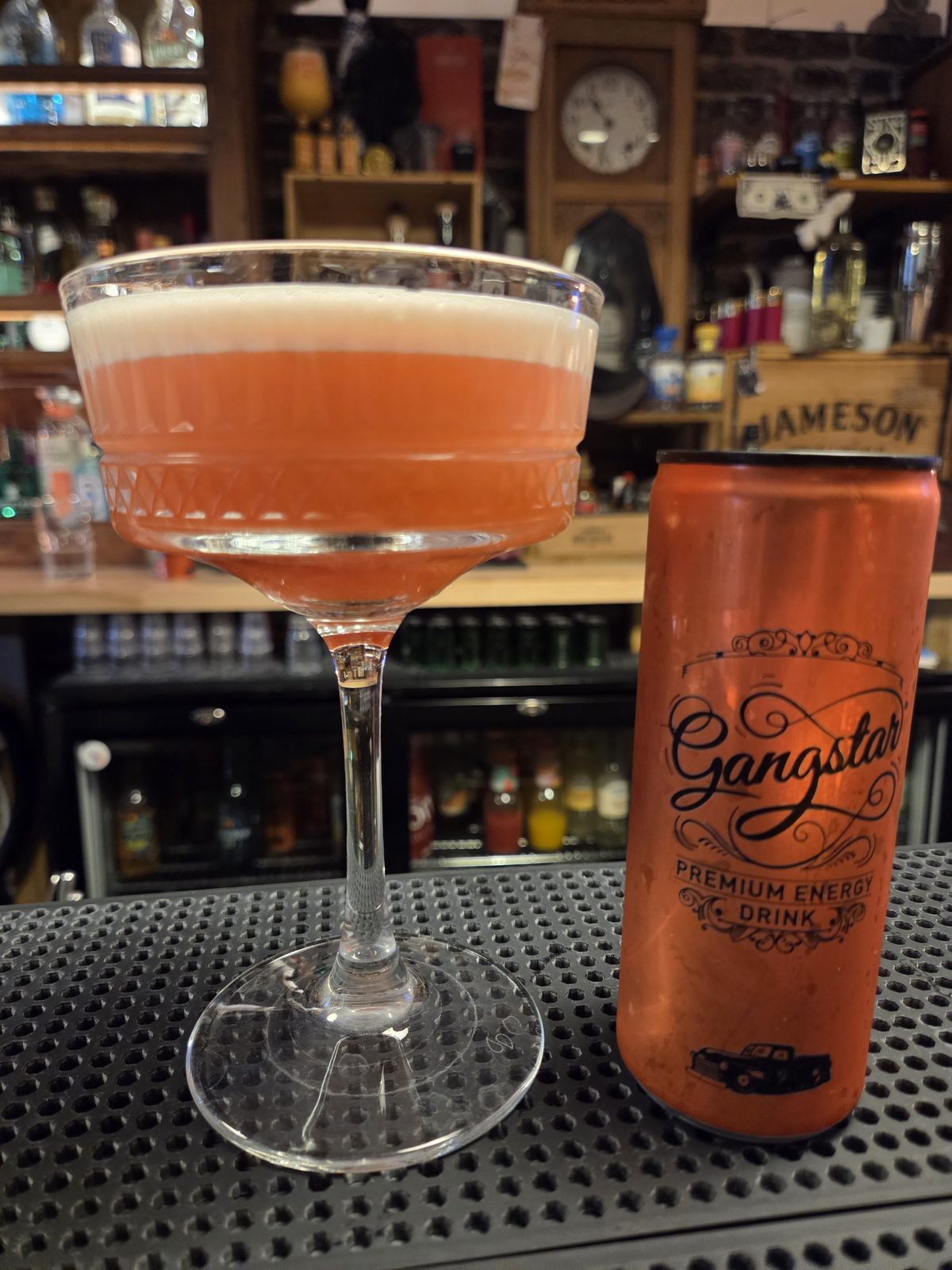 Le cocktail Ruby Heist, rose et mousseux dans une coupette, à côté d'une canette Gangstar